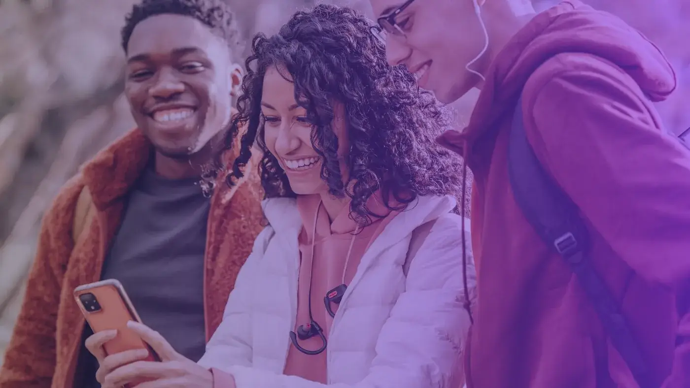 Trois étudiants souriants regardent un téléphone ensemble, au cœur d’une équipe réseaux sociaux